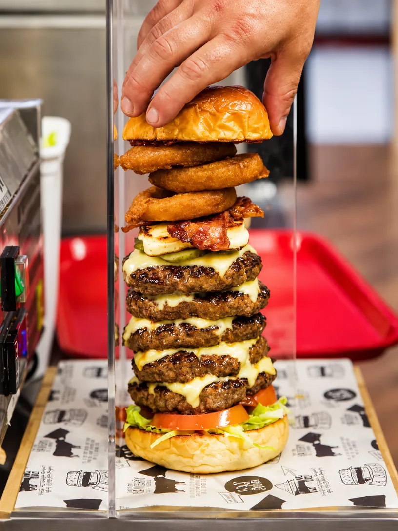 A tall stacked burger being assembled at Eat Burger